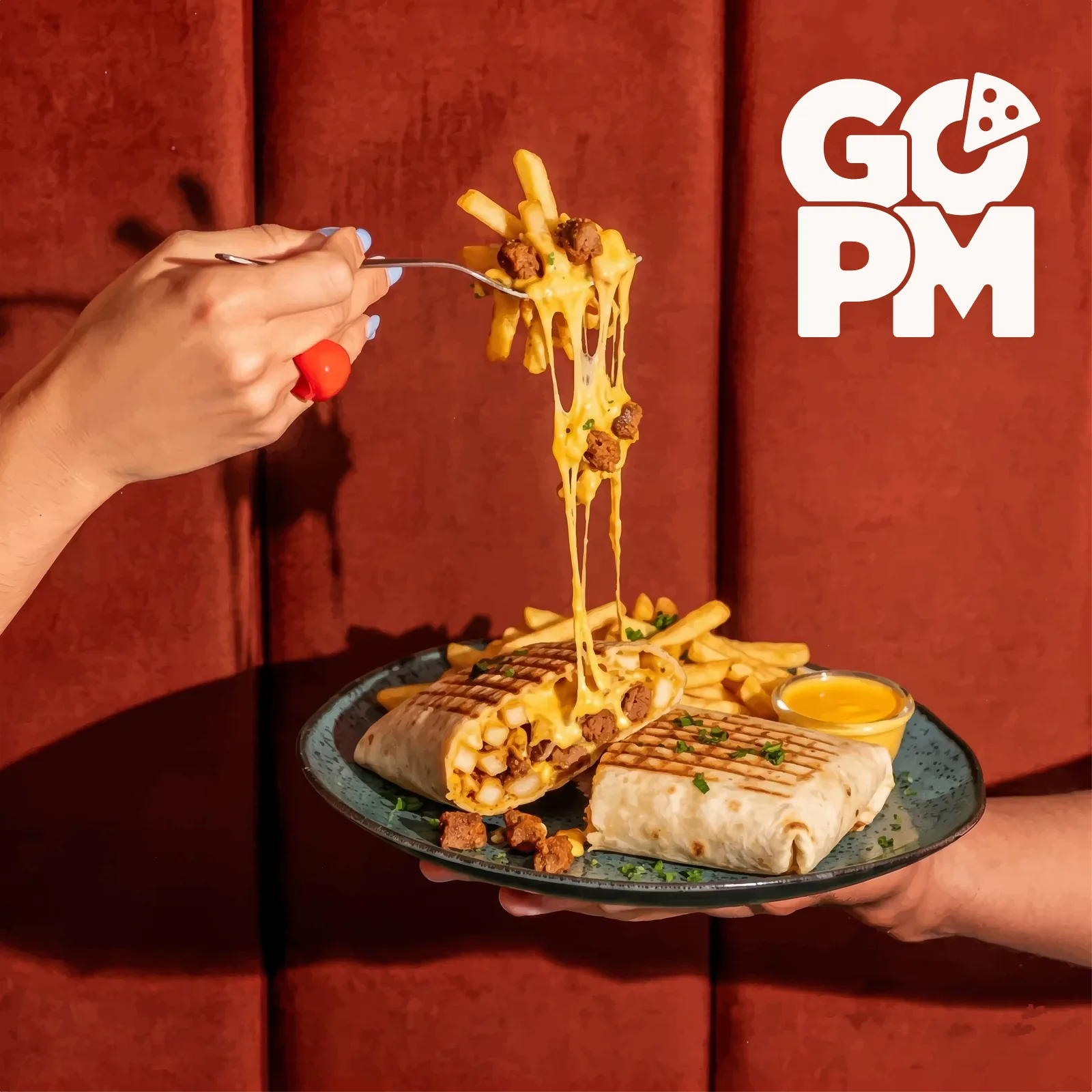 Gegrillter Wrap und Pommes mit geschmolzenem Käse, tiefroter Samt-Hintergrund mit GO-PM-Logo.